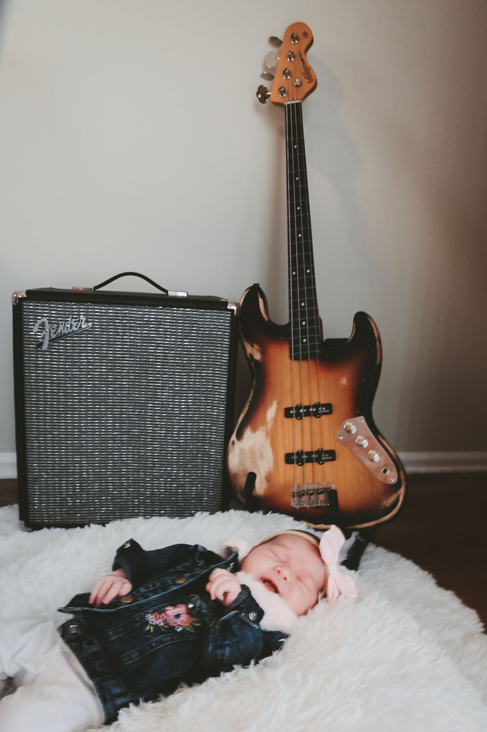 A vintage Fender bass guitar and amp set up with a sleeping baby on white fur.