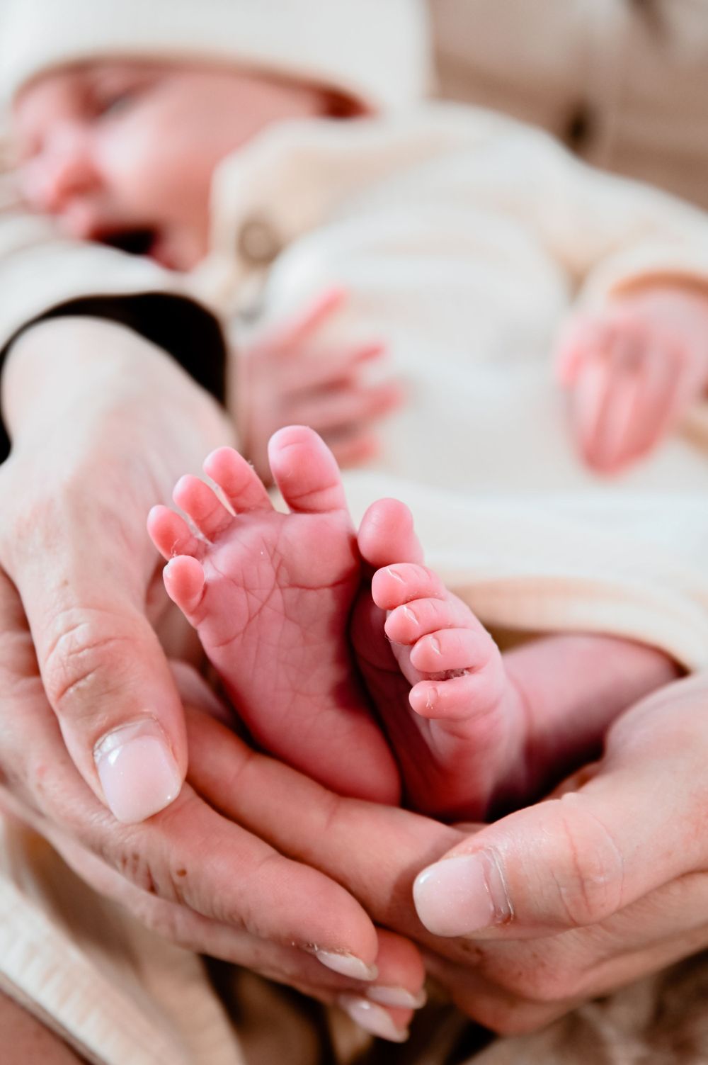 Close-up of tiny newborn baby feet being gently held in adult hands.