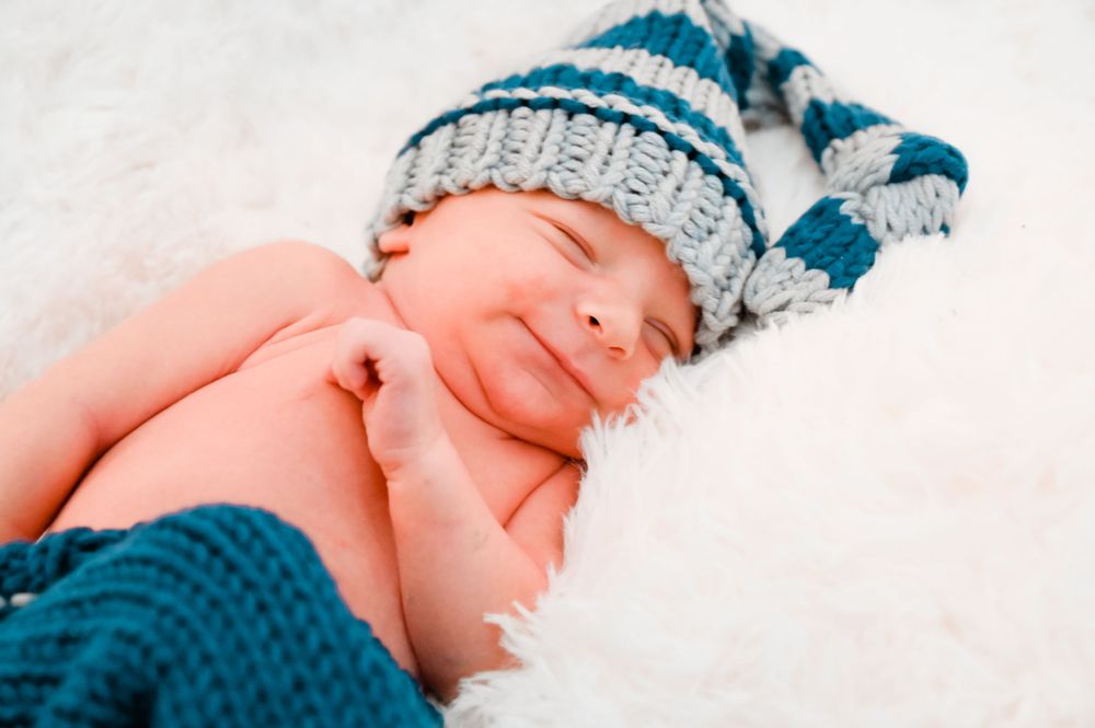 Baby wearing blue and gray knit hat sleeping on white background.