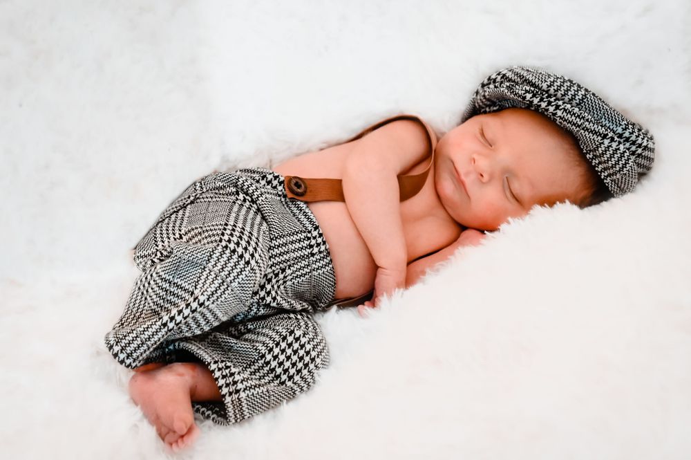 Baby napping in checkered outfit on white backdrop.