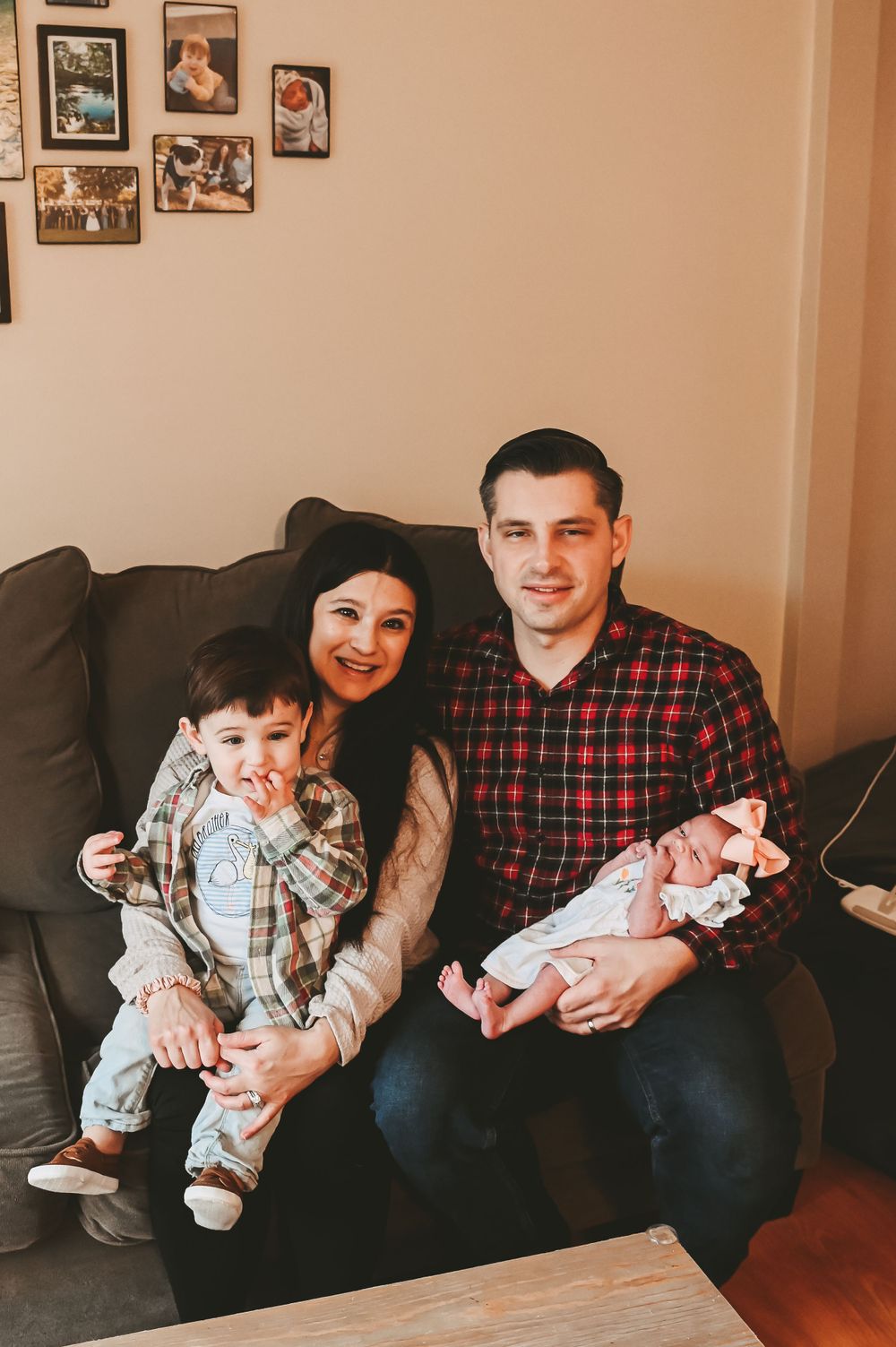 Family sitting together on couch for portrait with baby in casual home setting.