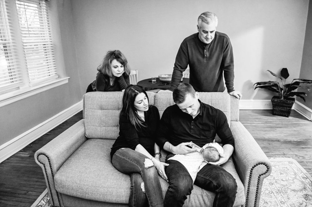 Black and white series showing a couple sitting on a couch sharing intimate moments with their newborn.