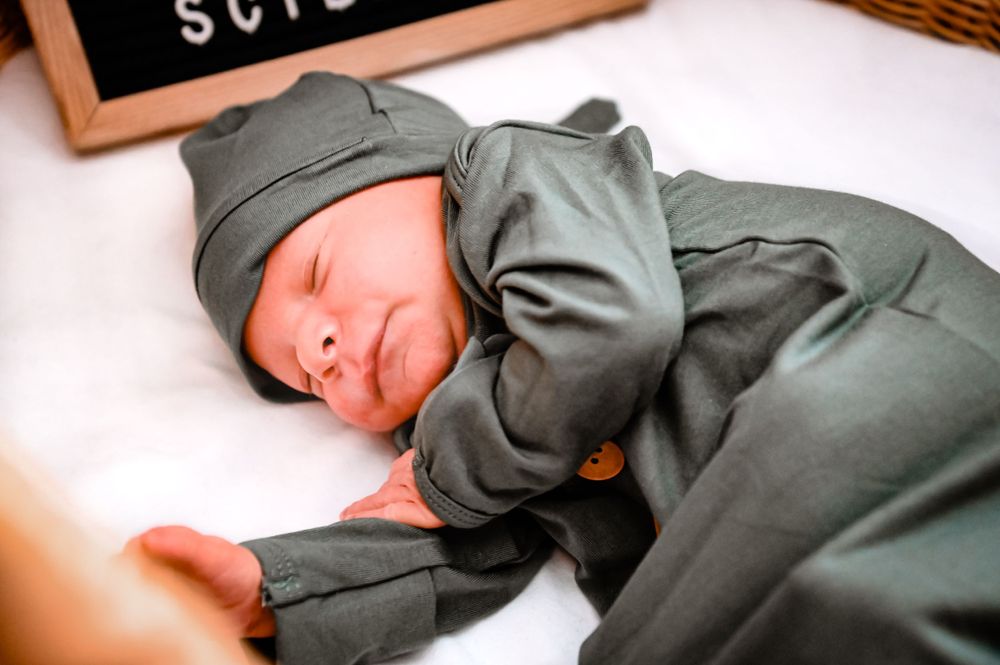 Baby sleeping peacefully in dark clothing on white background.