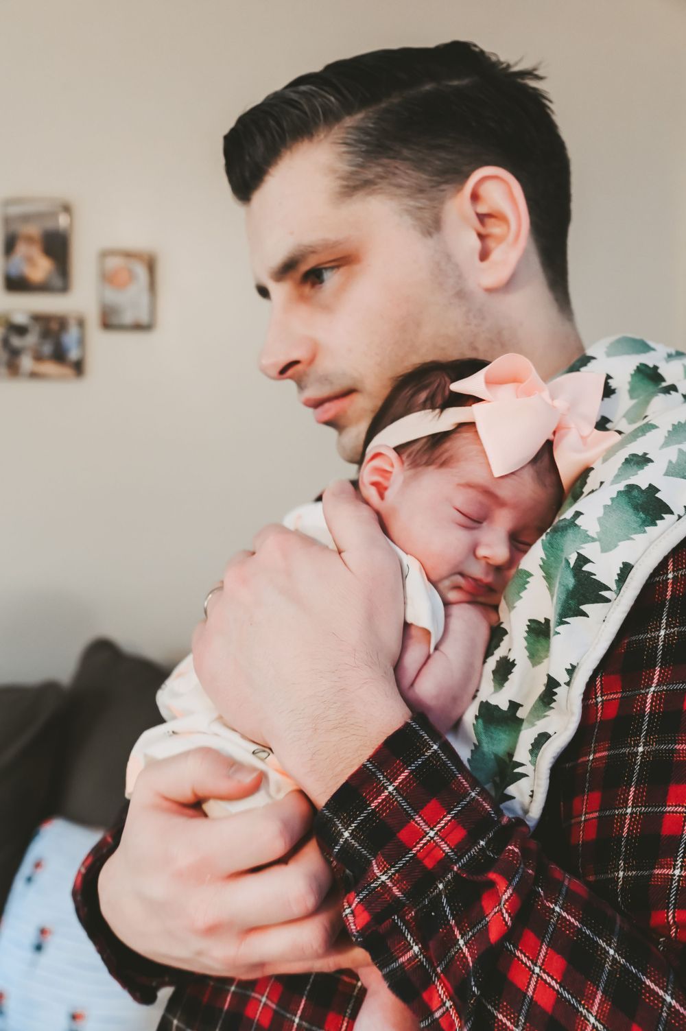 Parent in plaid shirt holding sleeping newborn baby wearing white bow headband.