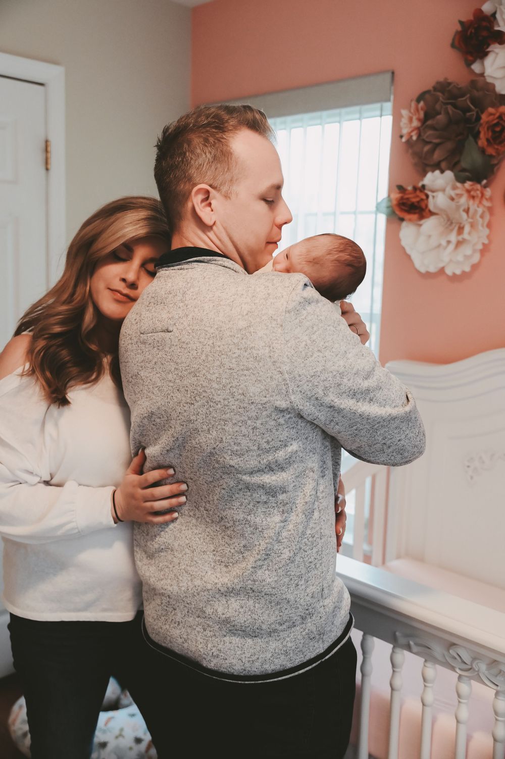 A family shares tender embraces in a nursery with coral colored walls.