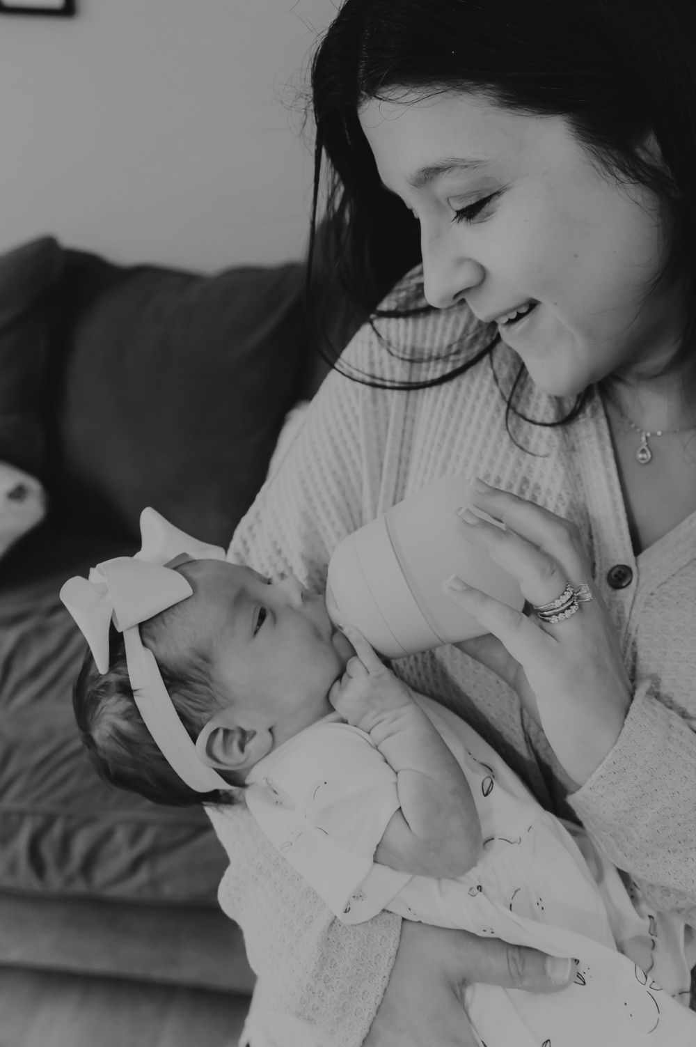 A tender black and white moment between parent and newborn baby wrapped in white on a couch.