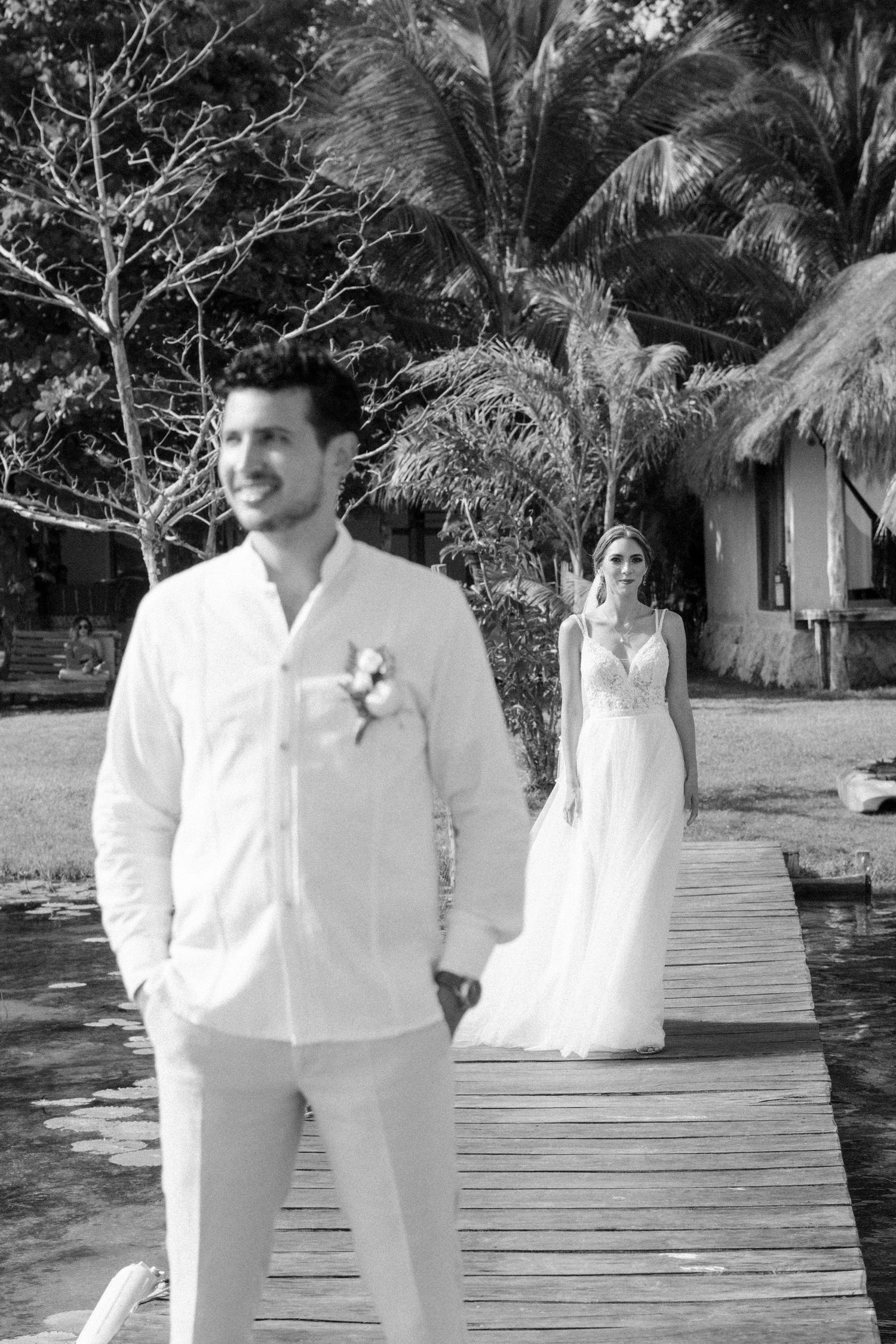 First look wedding photo on wooden deck with tropical palm trees in background.