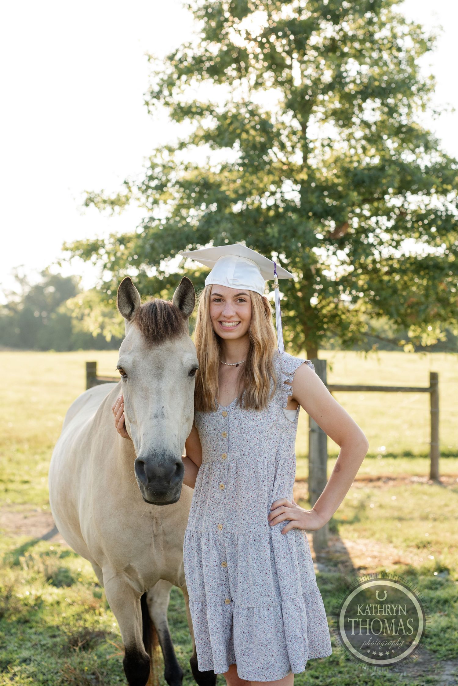 Graduate in a tiered dress poses with a friendly white horse at golden hour.