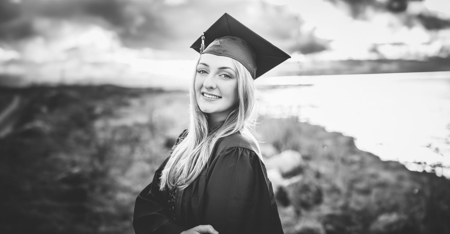 Young woman in graduation cap and gown smiling outdoors, captured in one a senior picture portrait session
