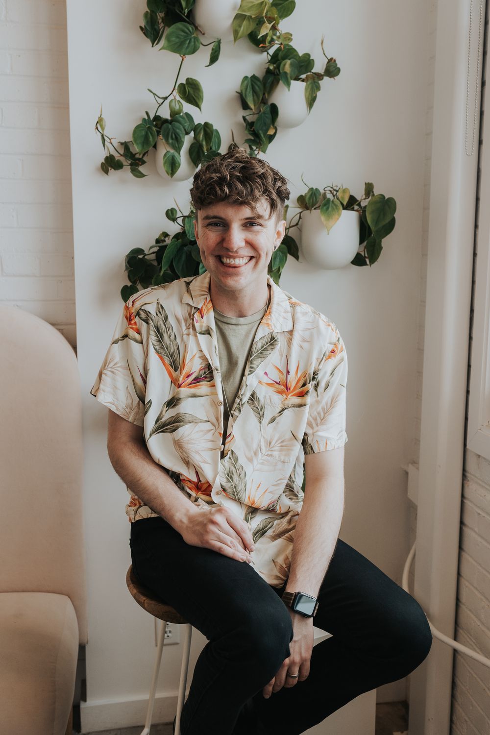 Indoor portrait with tropical print shirt against white wall with climbing plants.