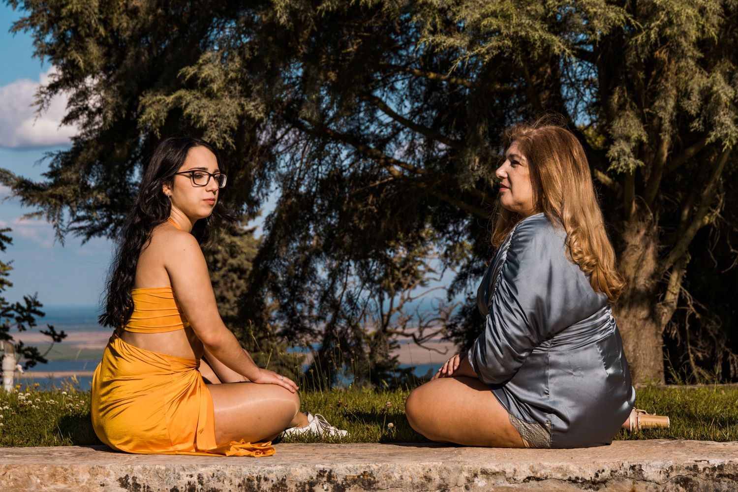 Friends lounging on stone wall against backdrop of evergreen trees.
