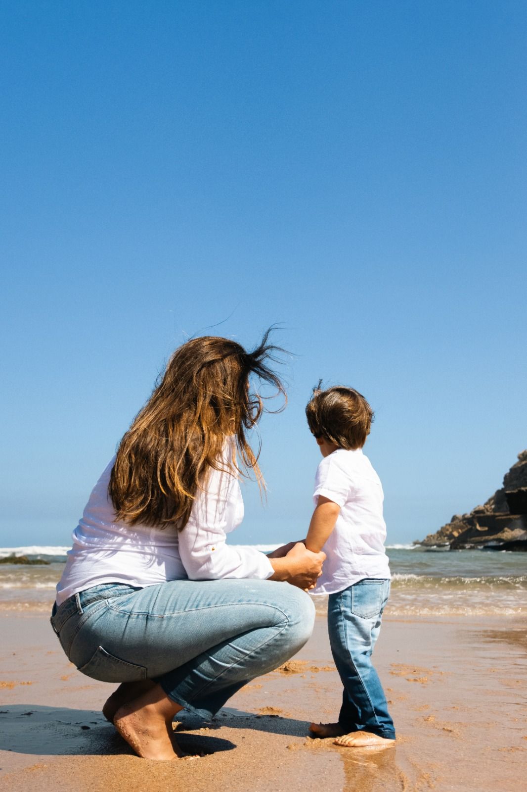 Two people crouching on a sandy beach examining something together.