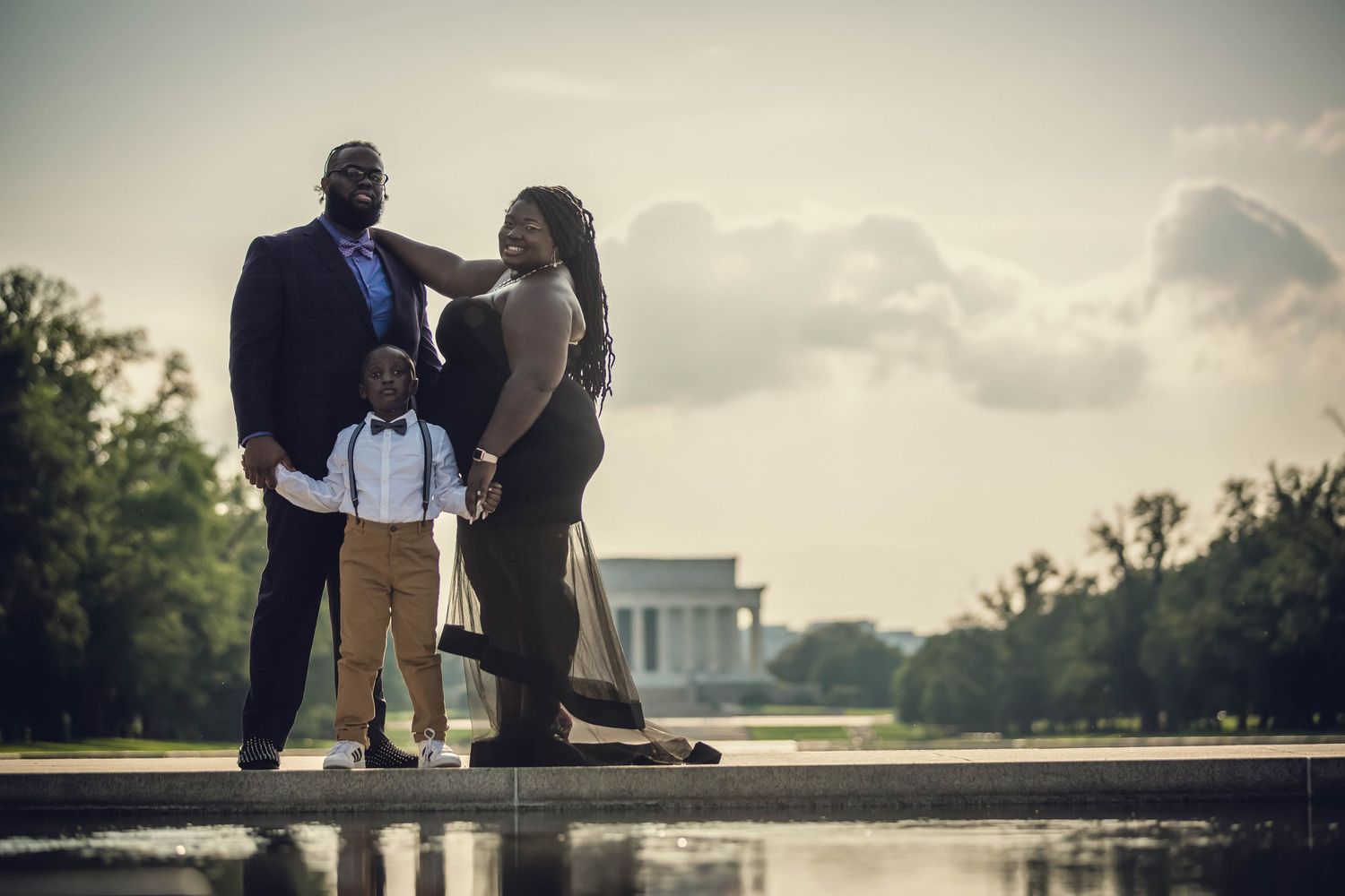 A family of three poses near the Reflecting Pool with the Lincoln Memorial in the background at dusk.