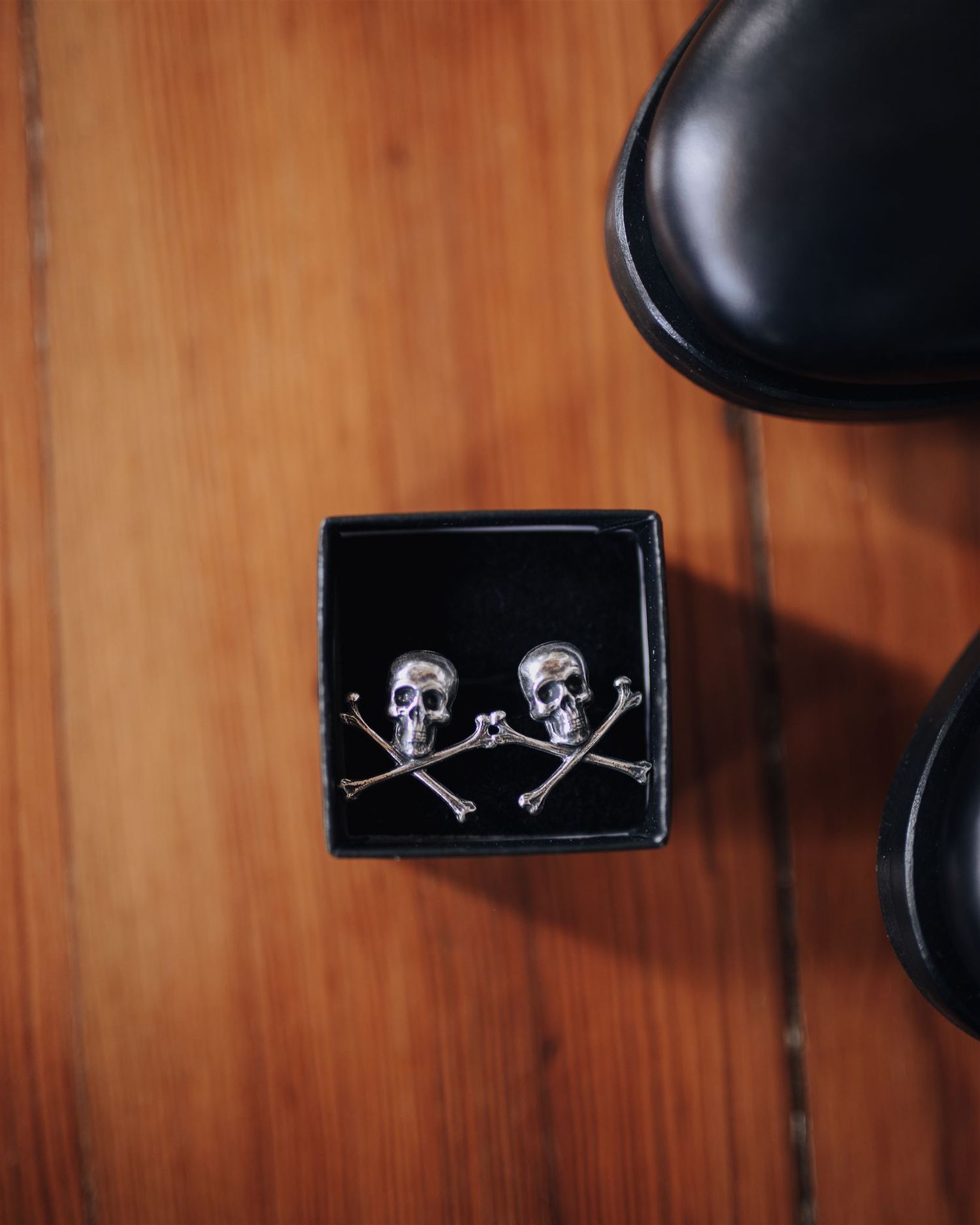 Black box containing skull and crossbones cufflinks on wooden surface.
