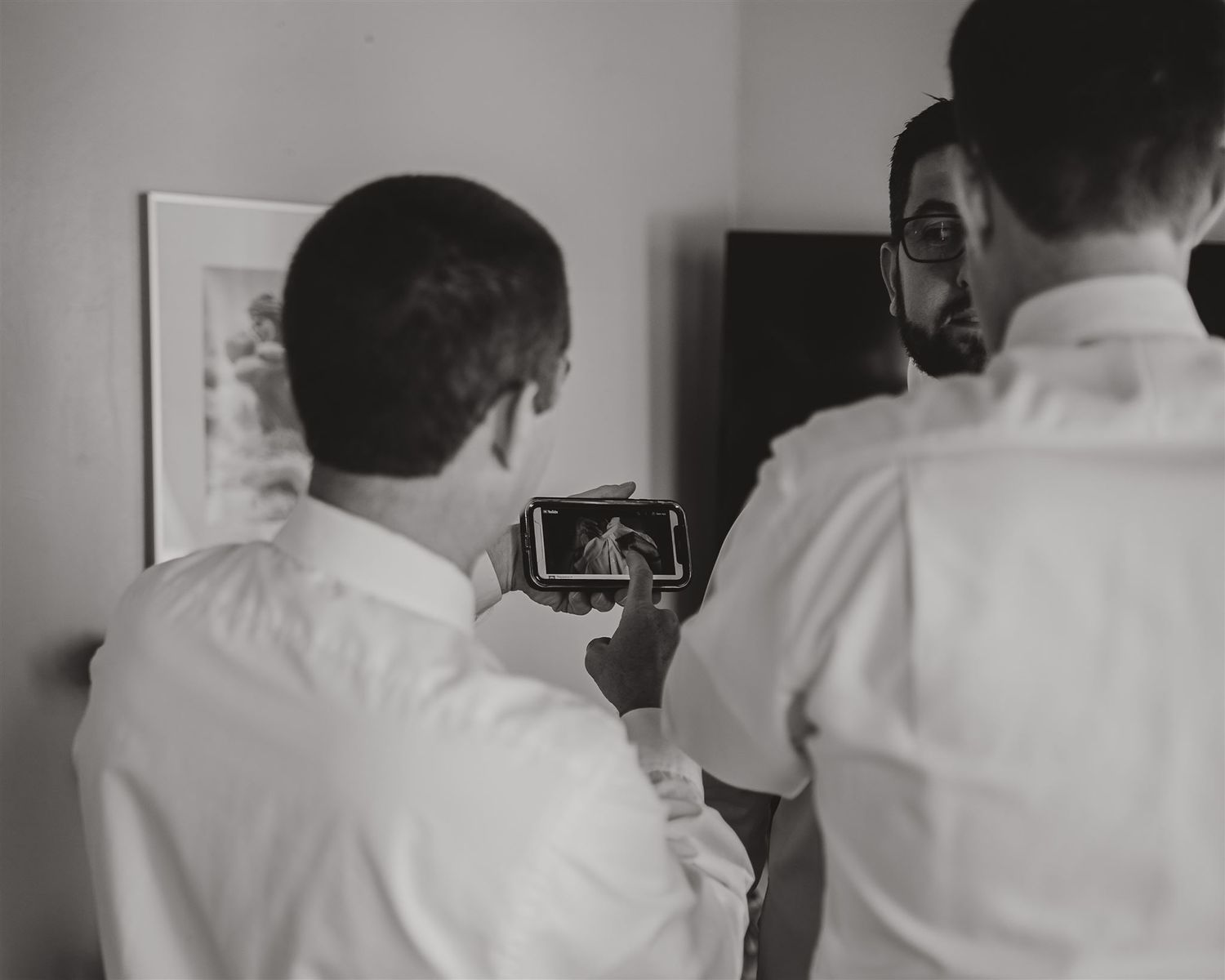 Two people in white shirts looking at a phone screen in a dimly lit room.
