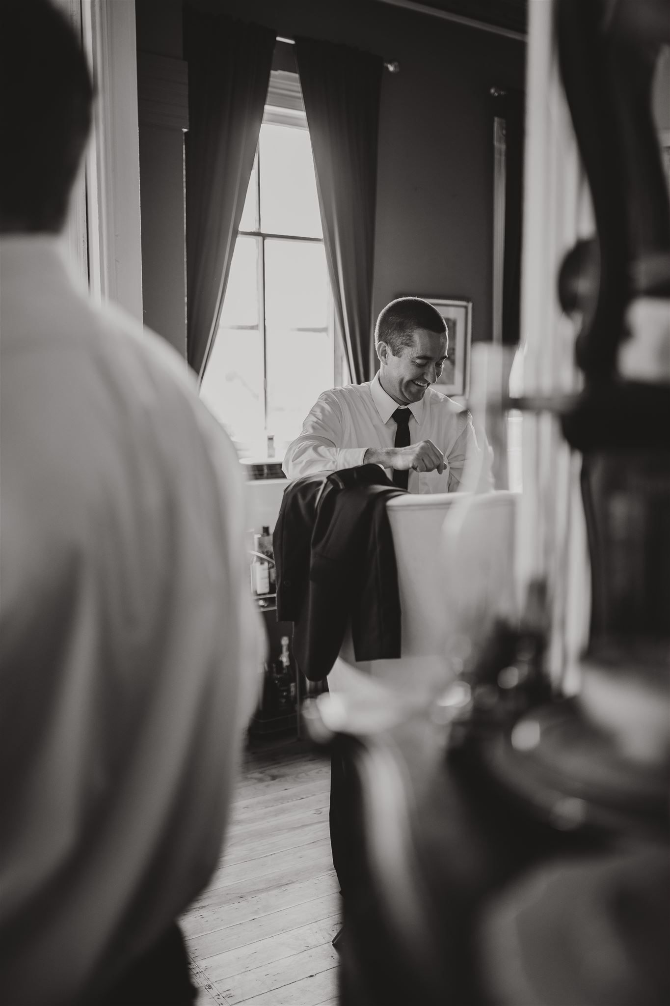 Black and white image of someone getting ready in formal attire by a window.