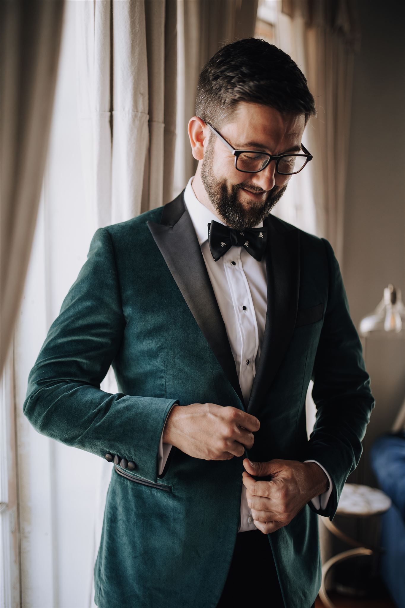 Person wearing emerald velvet tuxedo and bowtie smiles while adjusting jacket.