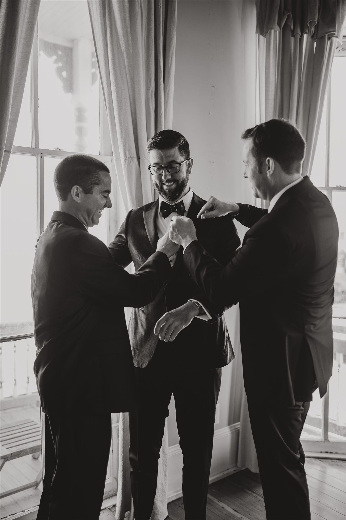 Three people in formalwear having a conversation by a window in black and white.