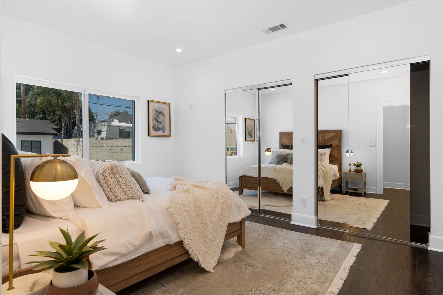 Modern bedroom with mirrored closet doors, wooden bed frame, hanging pendant light and neutral decor.