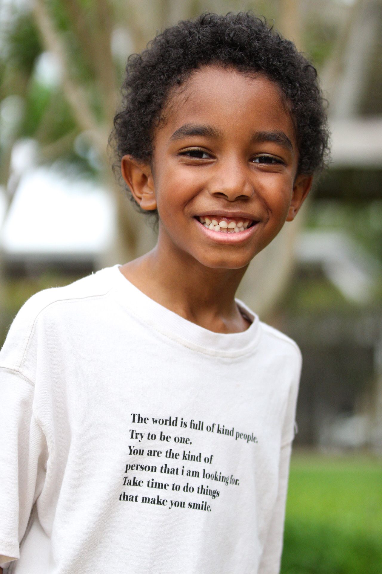Young person in white t-shirt with inspirational quote smiles at camera.