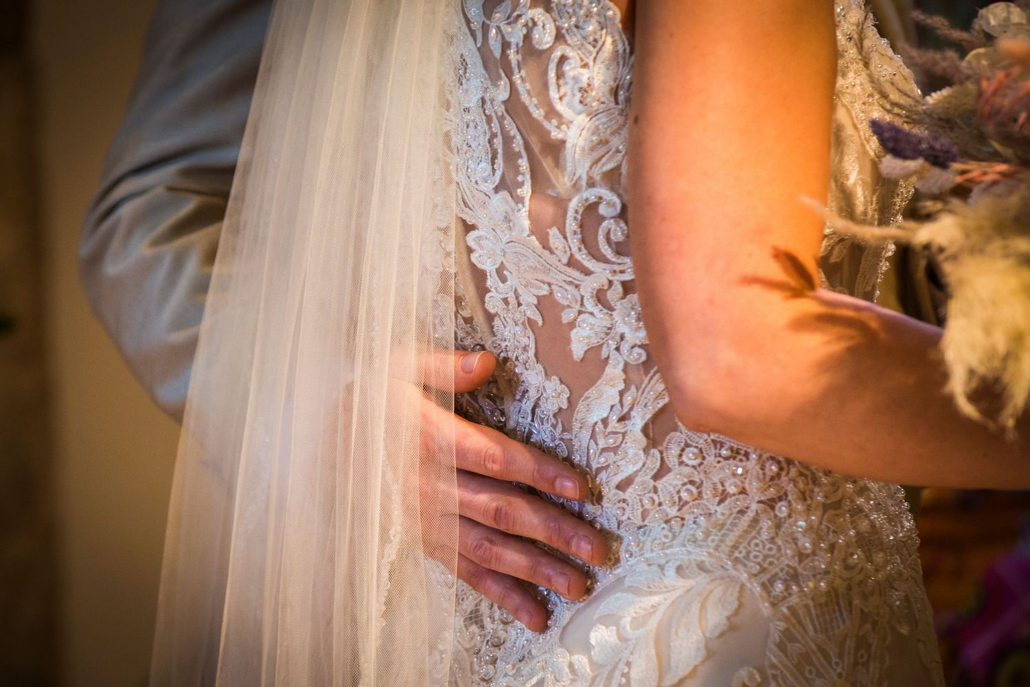 Close-up details of a lace wedding dress in warm lighting during the ceremony.
