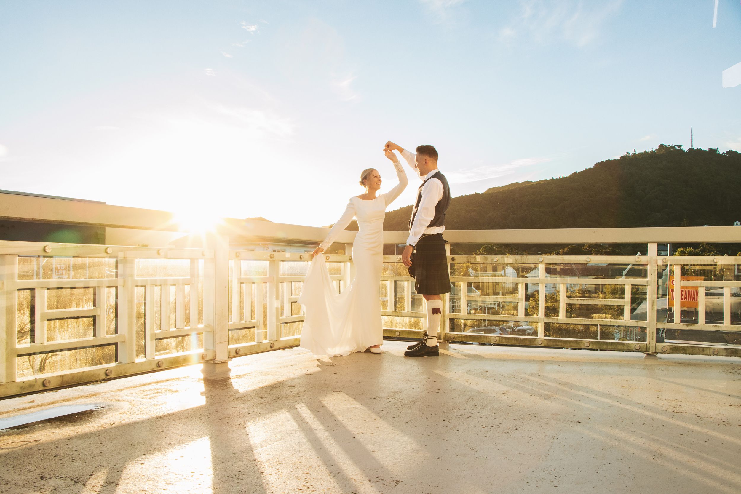 A couple shares a romantic moment on a wooden deck at sunset with mountains in the background.