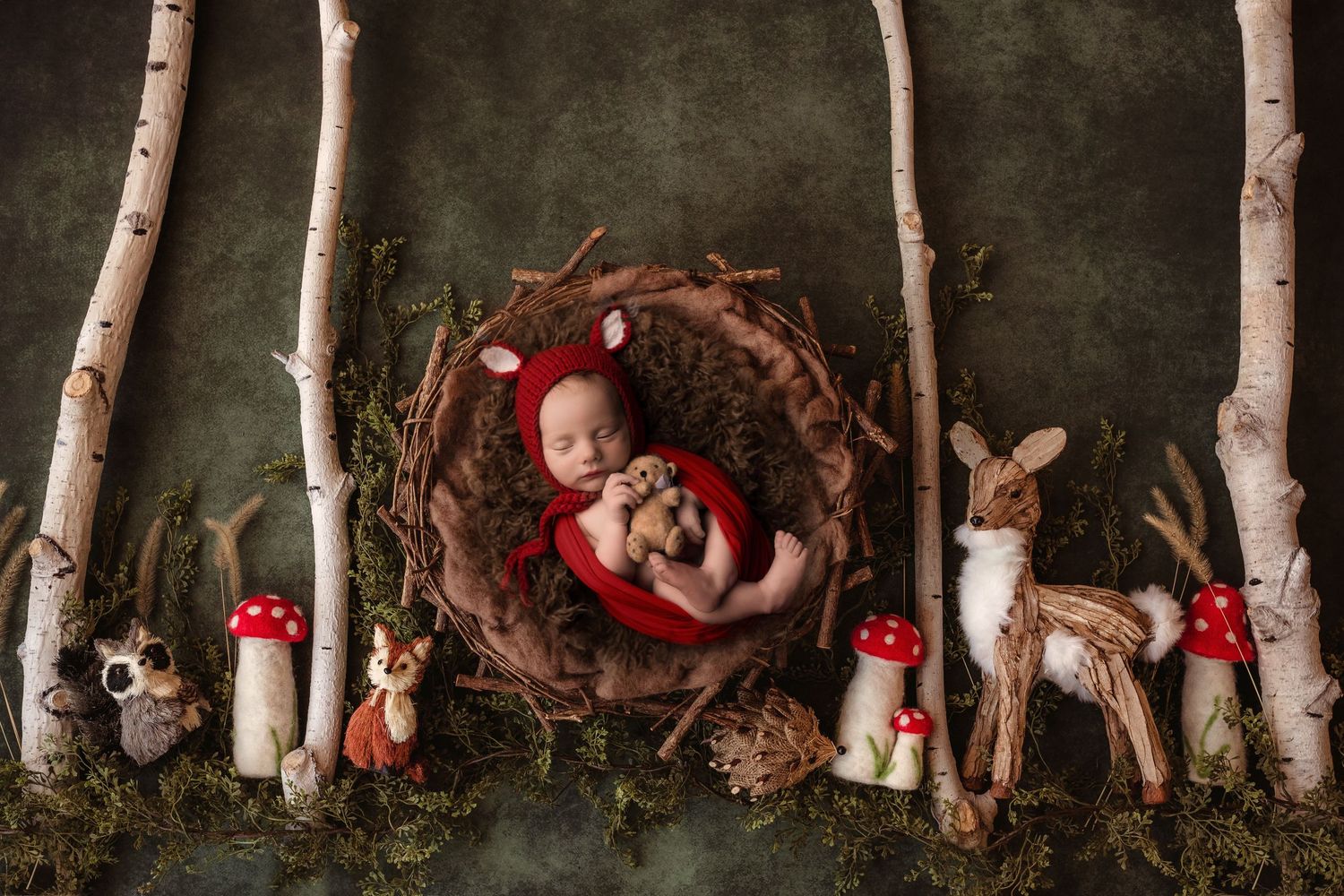 Whimsical woodland nursery scene with baby in red wrap surrounded by mushrooms and forest creatures.