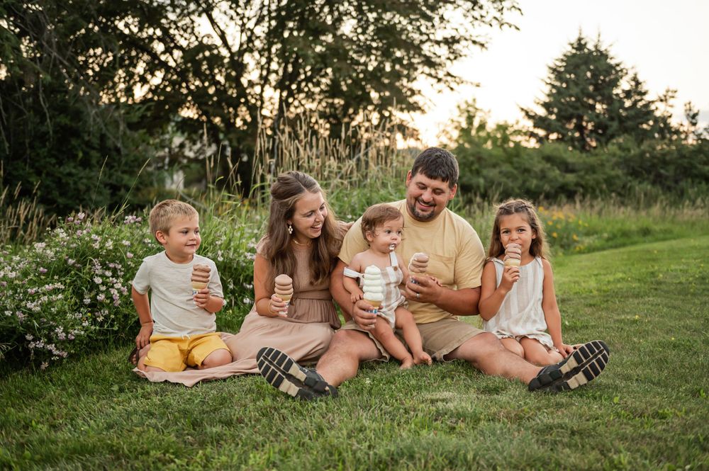 A family sits together on a blanket enjoying a summer evening picnic in a grassy field.