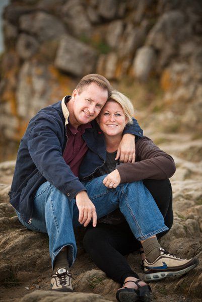 Couple sitting together on rocky outcrop during outdoor photo session.