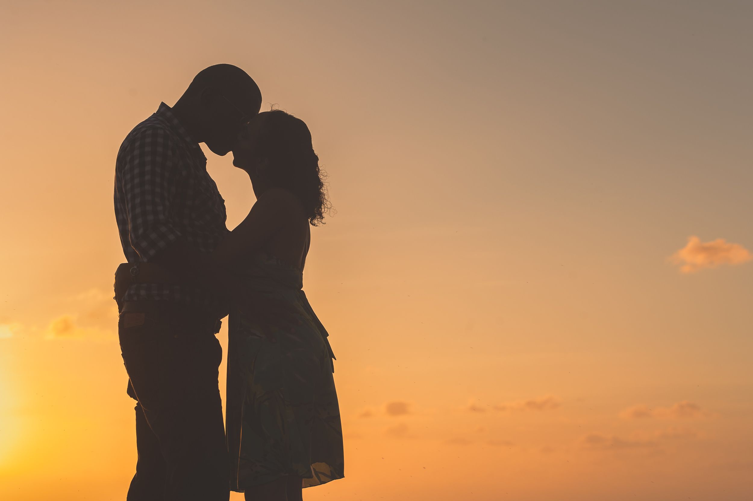 Silhouetted couple embracing against orange sunset sky.