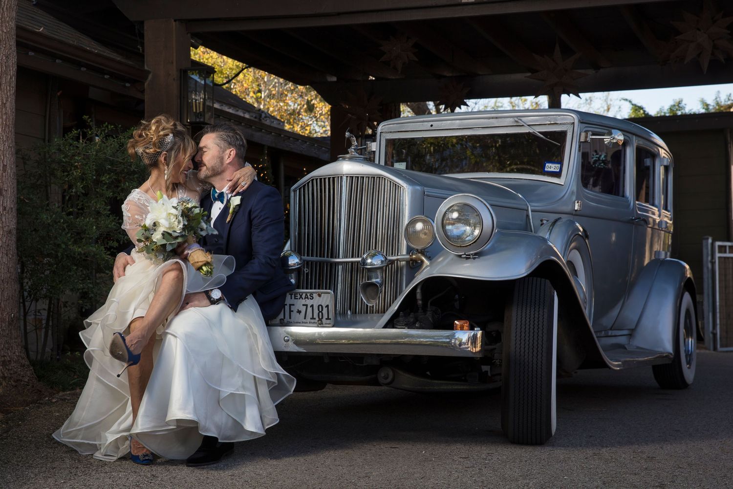 Classic vintage grey car decorated for a wedding celebration under a covered area.