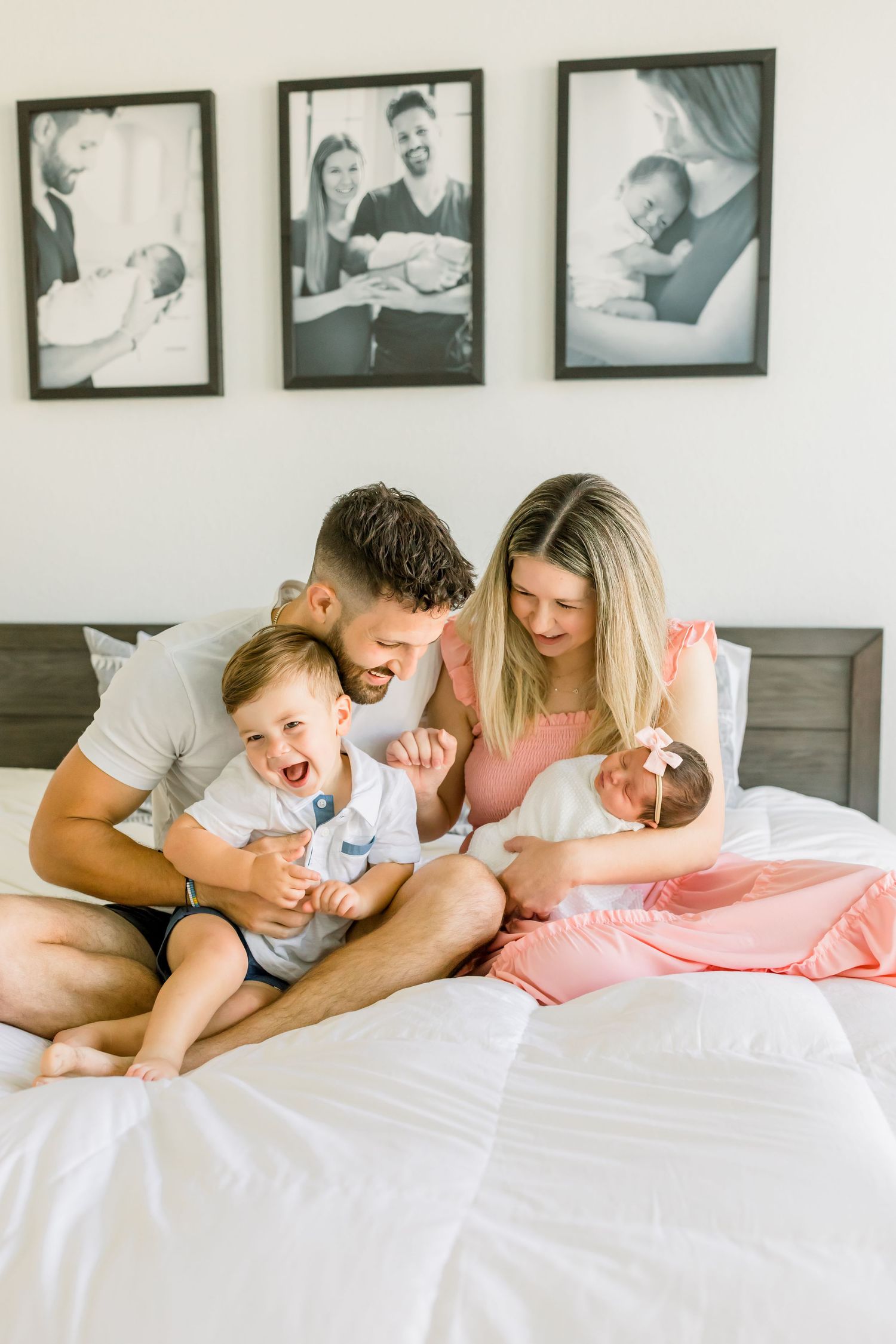 A joyful family moment captured on a white bed with vintage photos decorating the wall.
