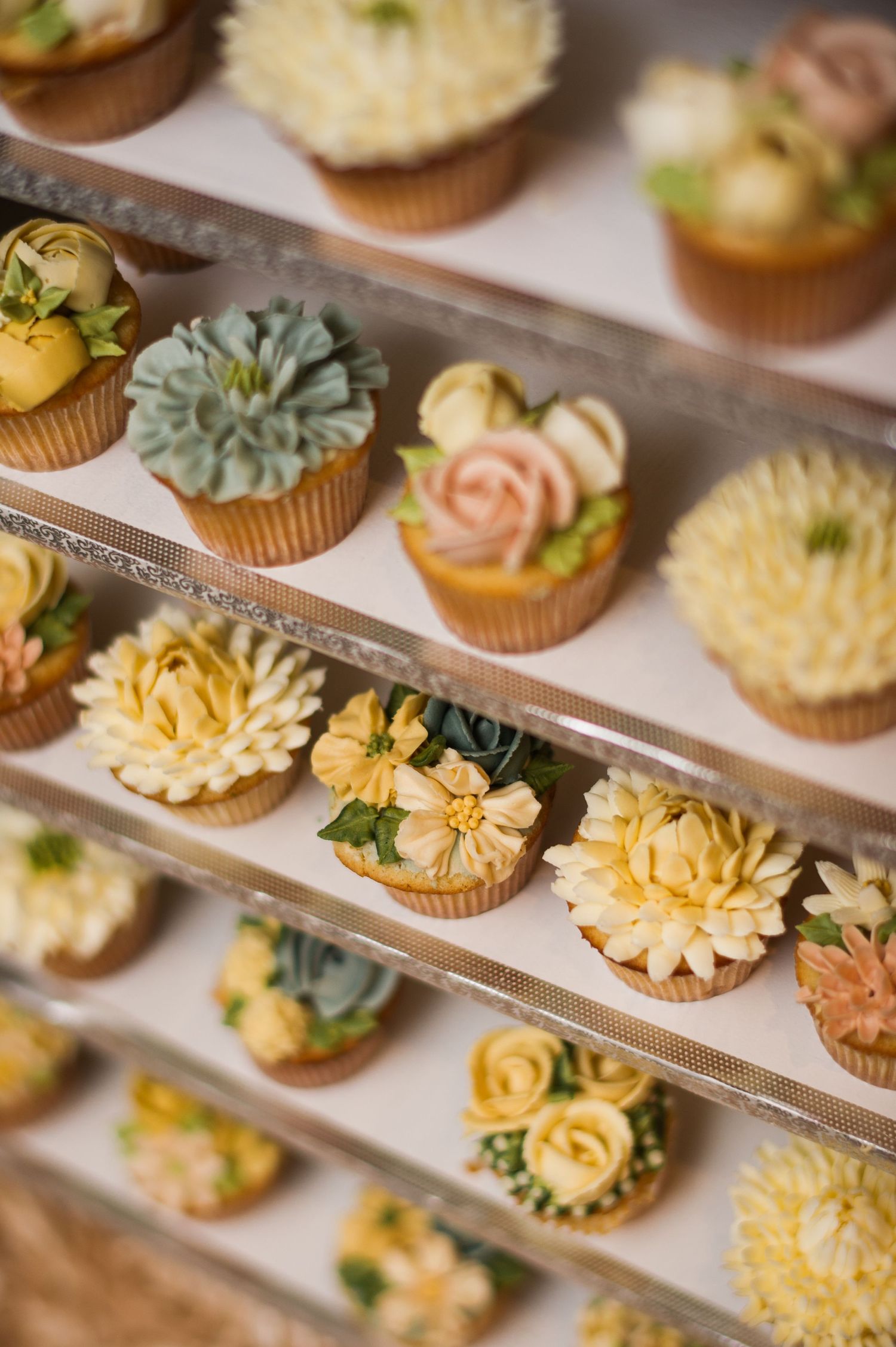 Display of beautifully decorated cupcakes with floral buttercream designs in pastel colors.
