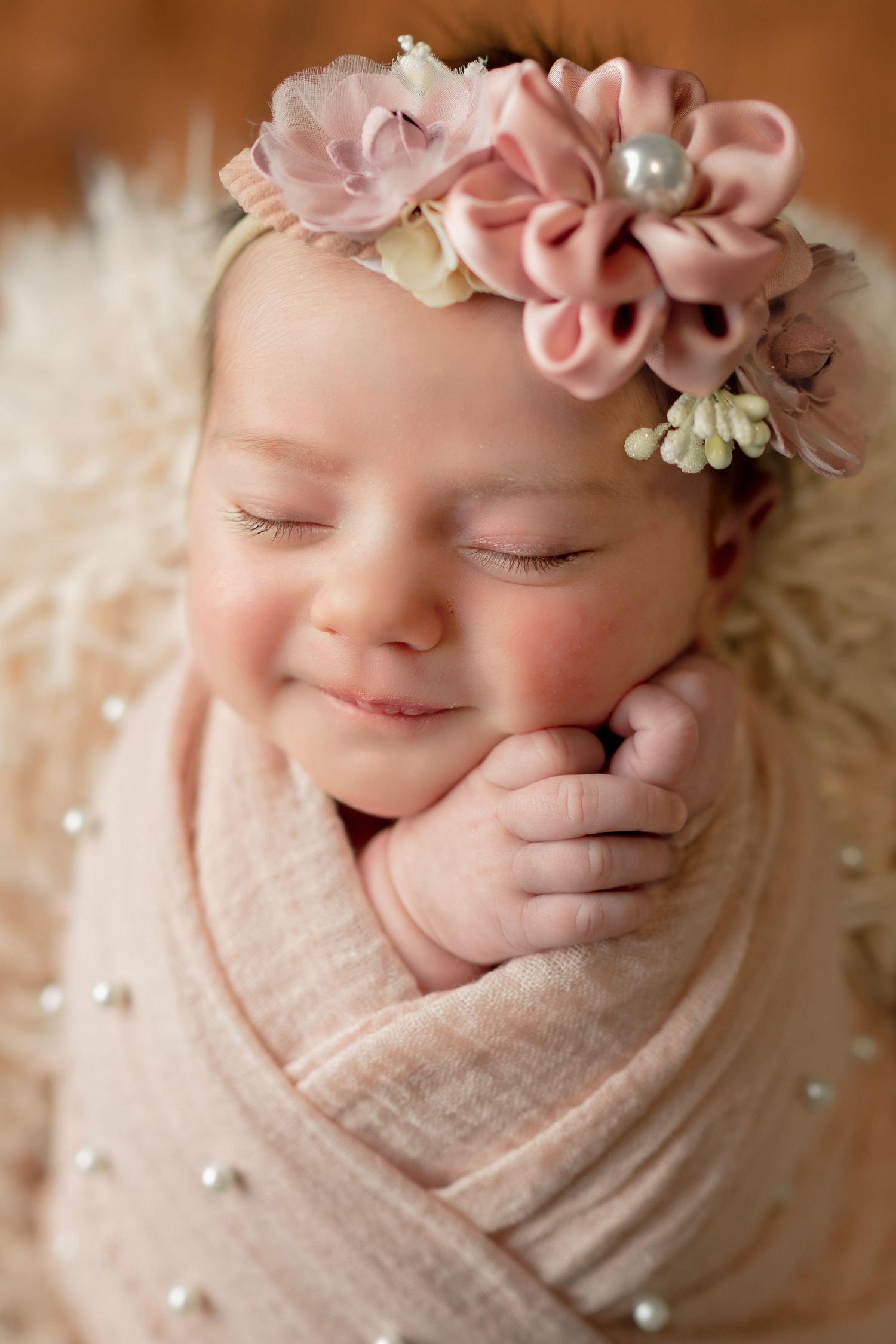 Peaceful newborn portrait with delicate pink floral crown and soft wrapping.