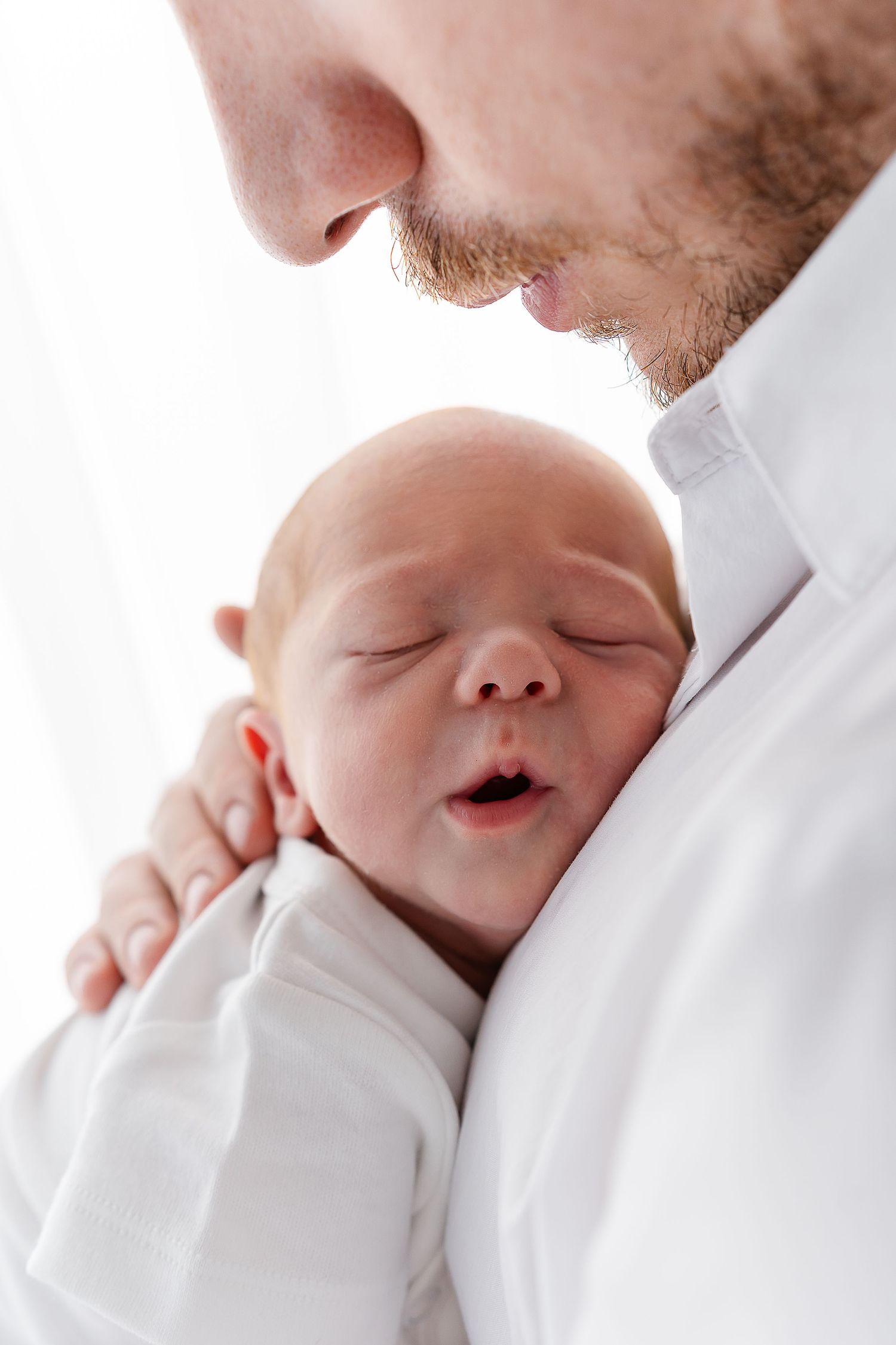 A sleeping newborn baby rests peacefully against someone wearing white.