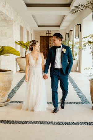 Wedding couple walking through elegant hallway with tiled floor and white stone walls.