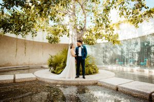 Wedding couple walking through garden pathway with stone walls and trees.