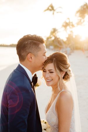 Romantic beach wedding portrait with golden sunset light filtering through palm trees.