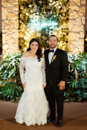 Wedding couple portrait session against stone wall with lush greenery and romantic lighting.