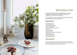 Elegant table setting with white flowers in dark vase alongside a black beans and rice recipe on cookbook pages.