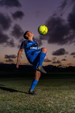 Soccer player performing trick moves with yellow ball against dramatic sunset sky.