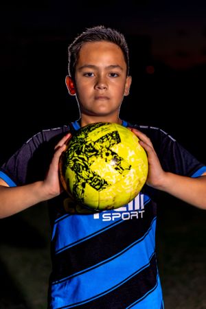 Dramatic low-light portrait of athlete holding illuminated soccer ball.