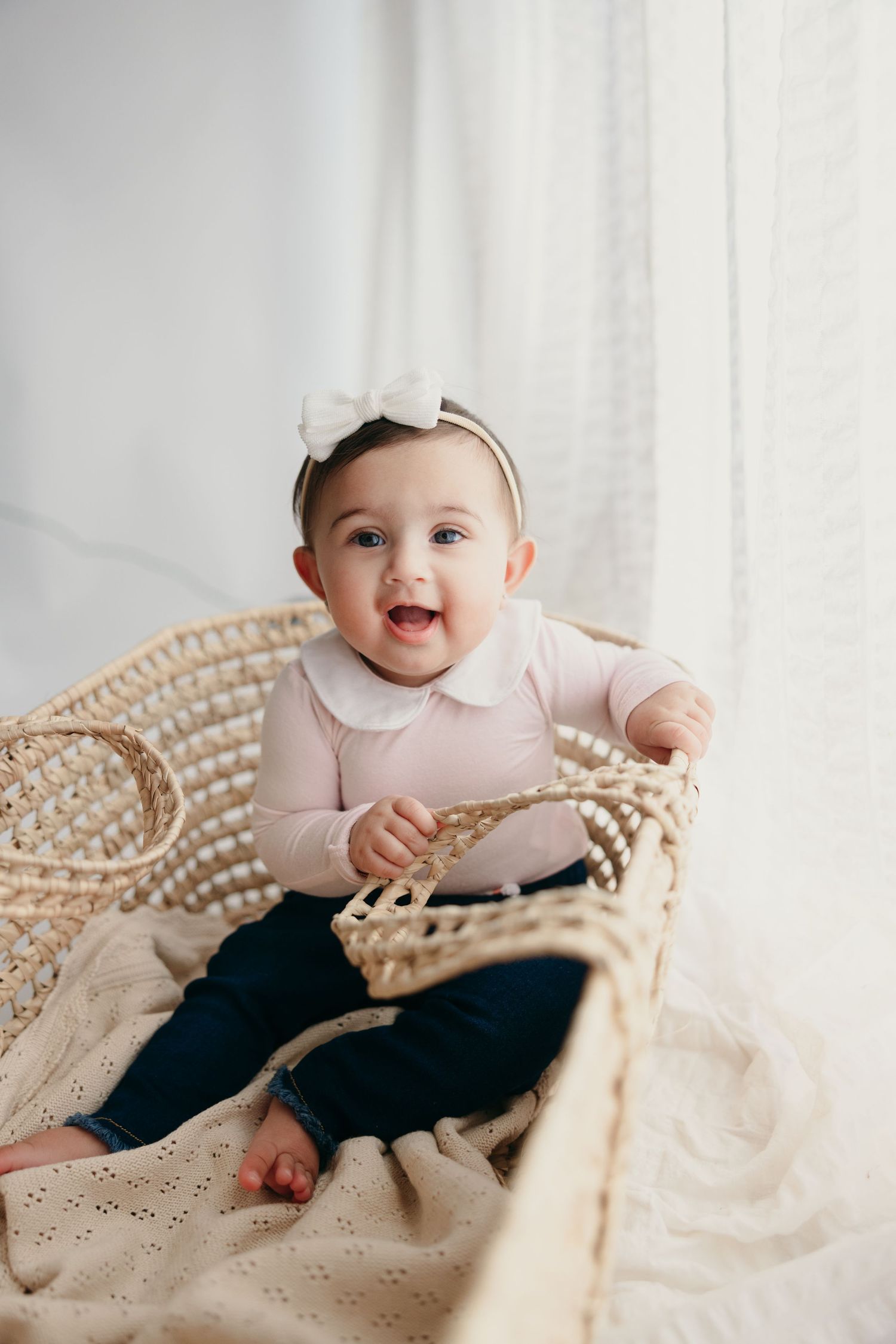 Happy baby in pink collared outfit sitting in woven basket.