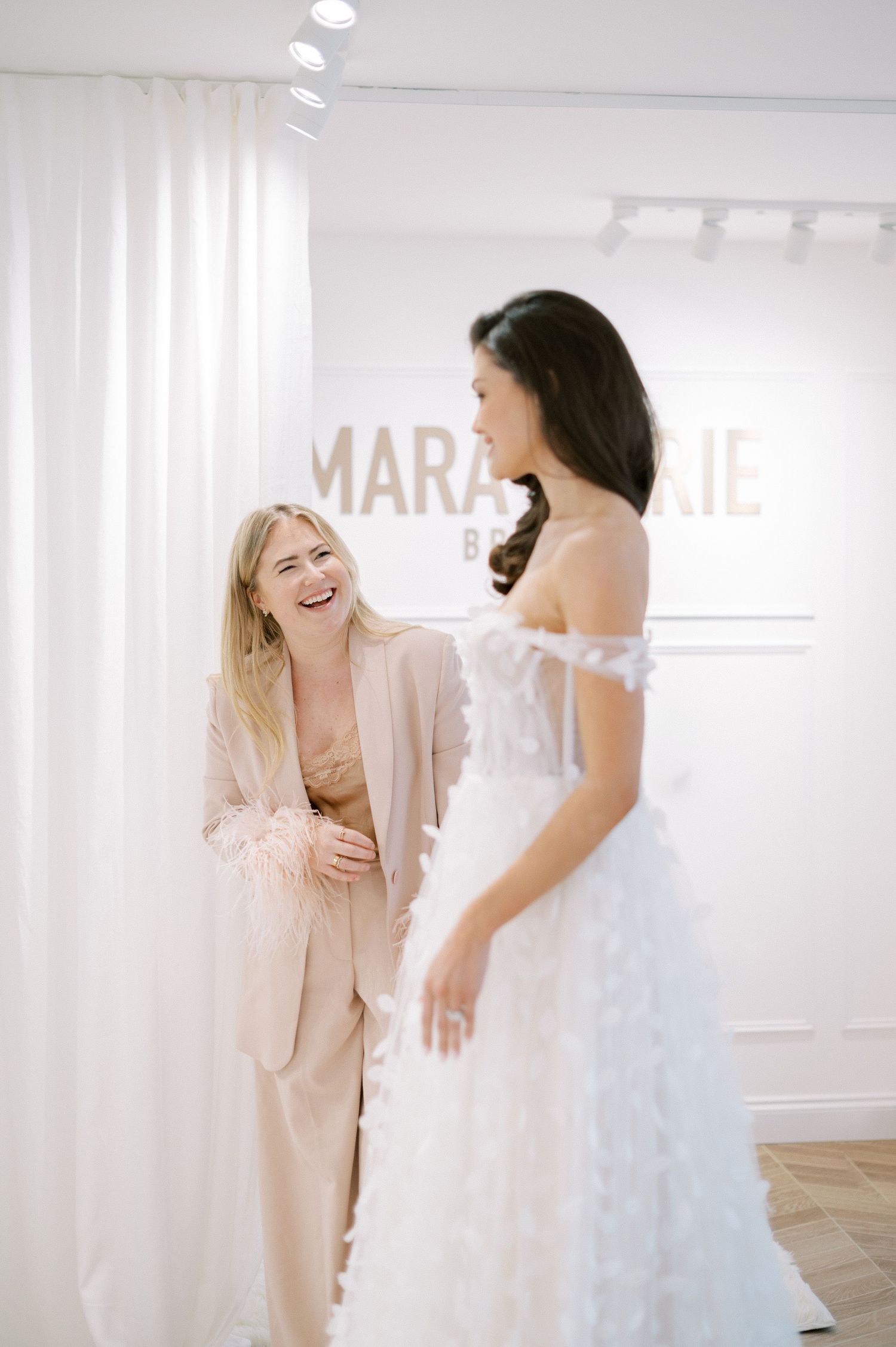Bright bridal boutique interior with white curtains and elegant wedding dresses on display.