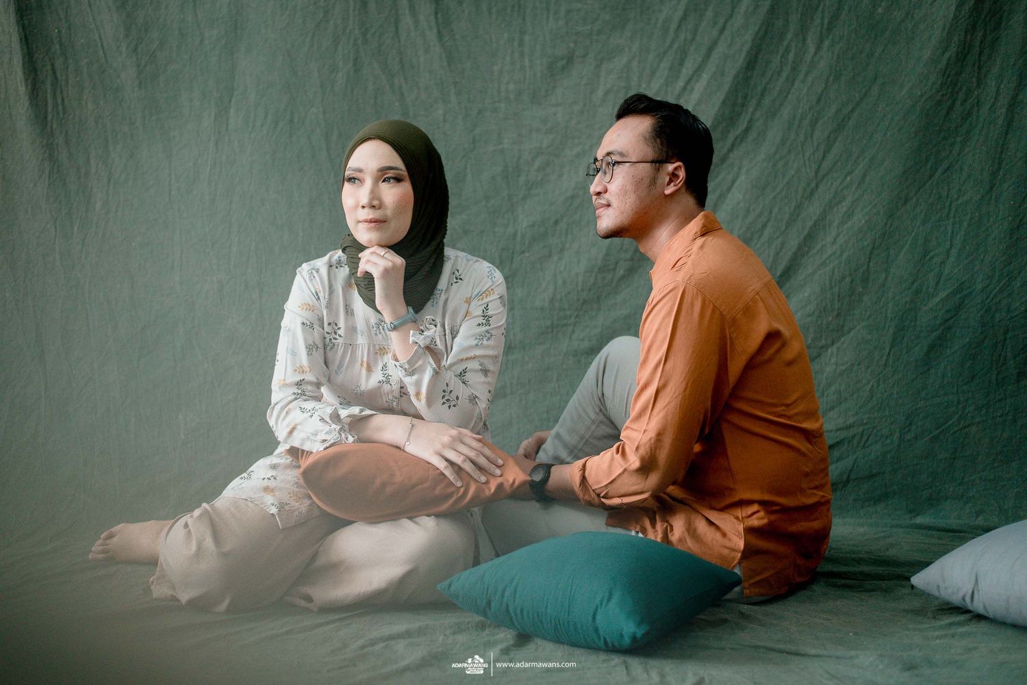 Couple sitting on floor having conversation against green textured backdrop.