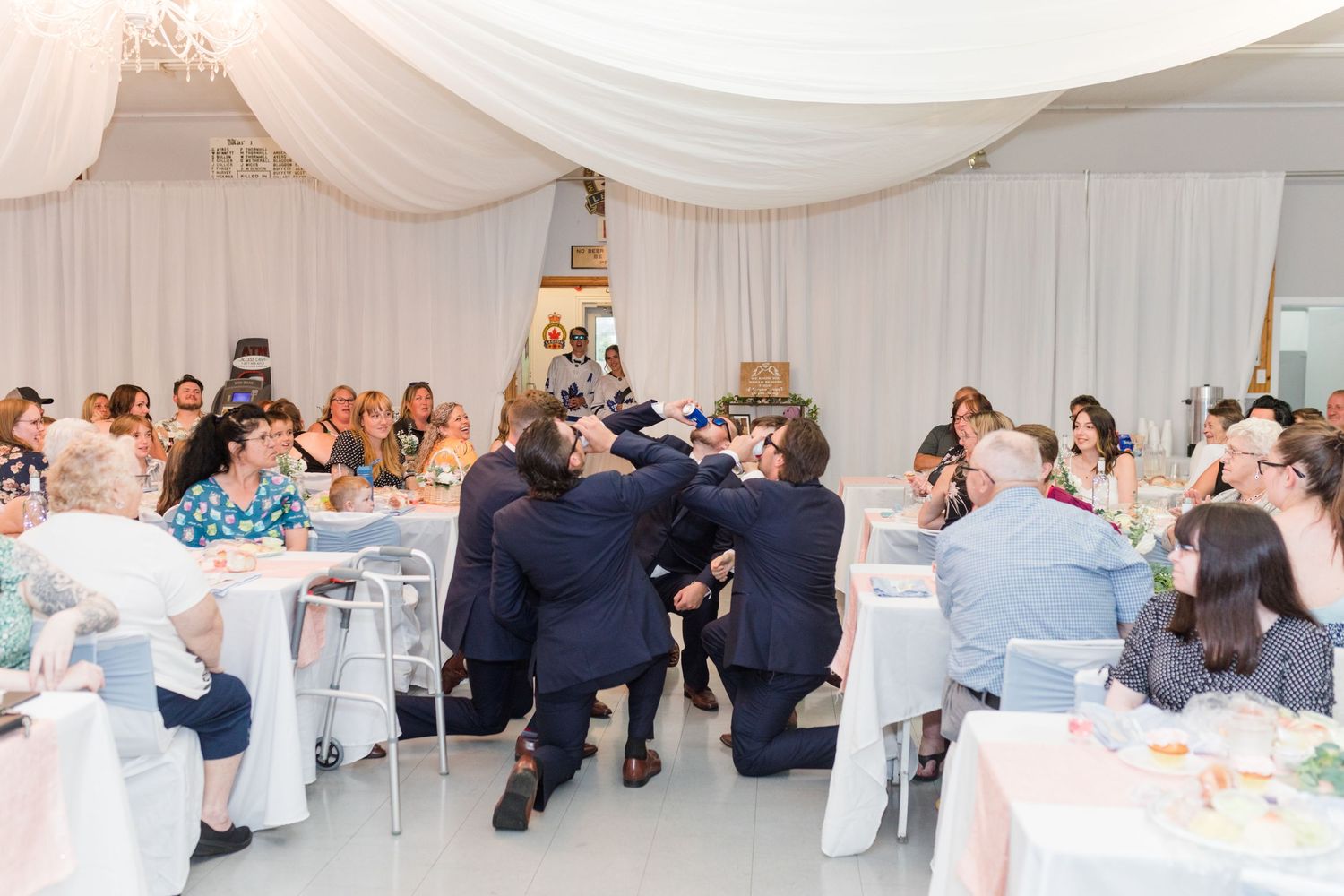 Wedding guests seated at decorated tables in an elegant white-draped reception hall.
