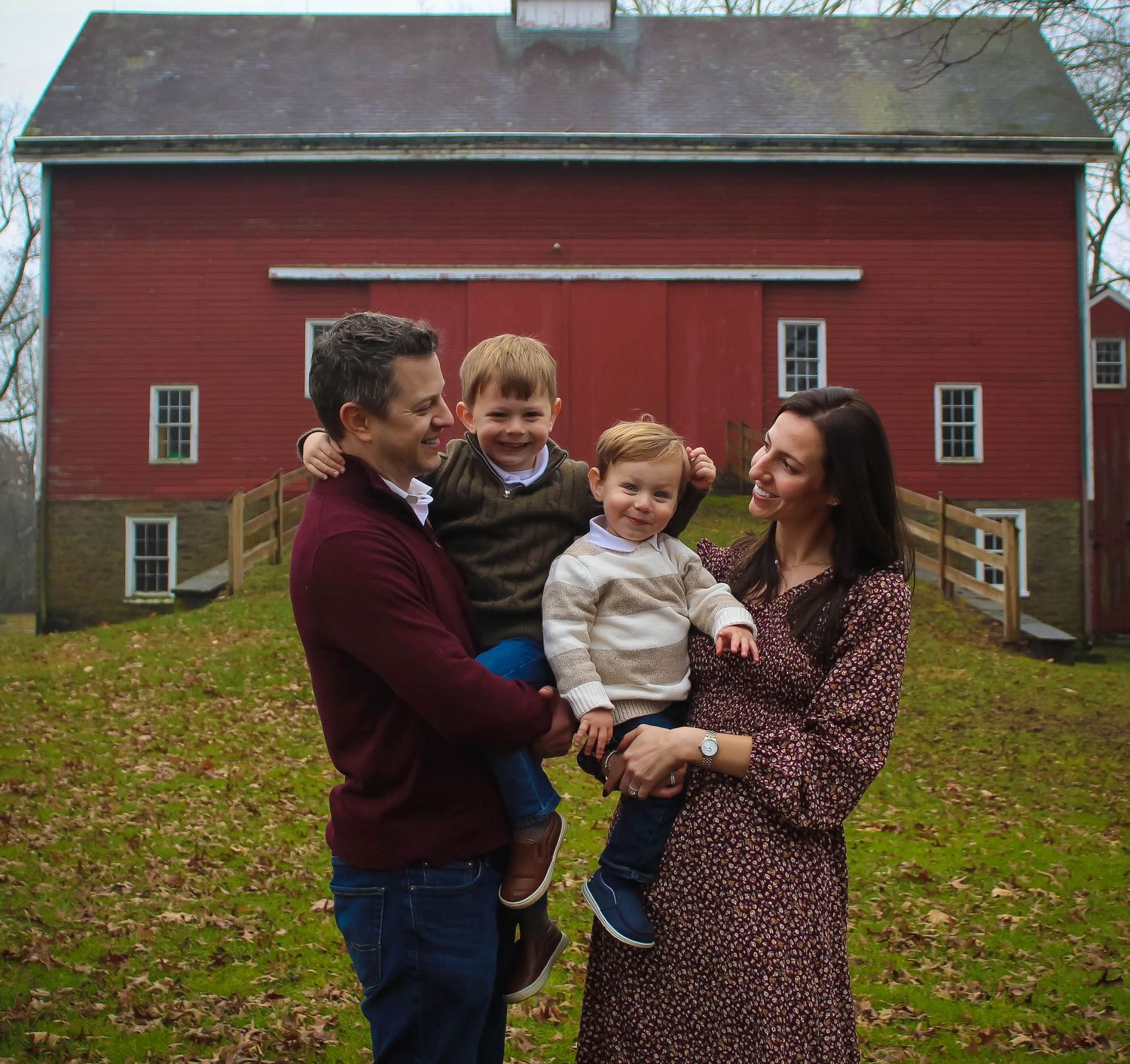 Family poses together outdoors against a classic red barn in autumn.
