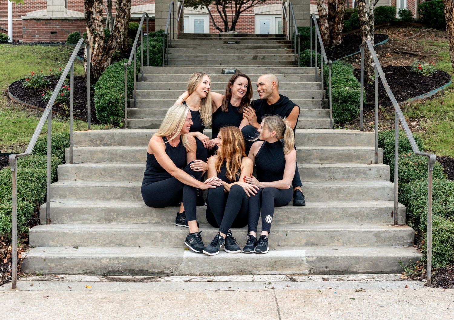 Group in matching black athletic wear poses casually on outdoor stone steps.