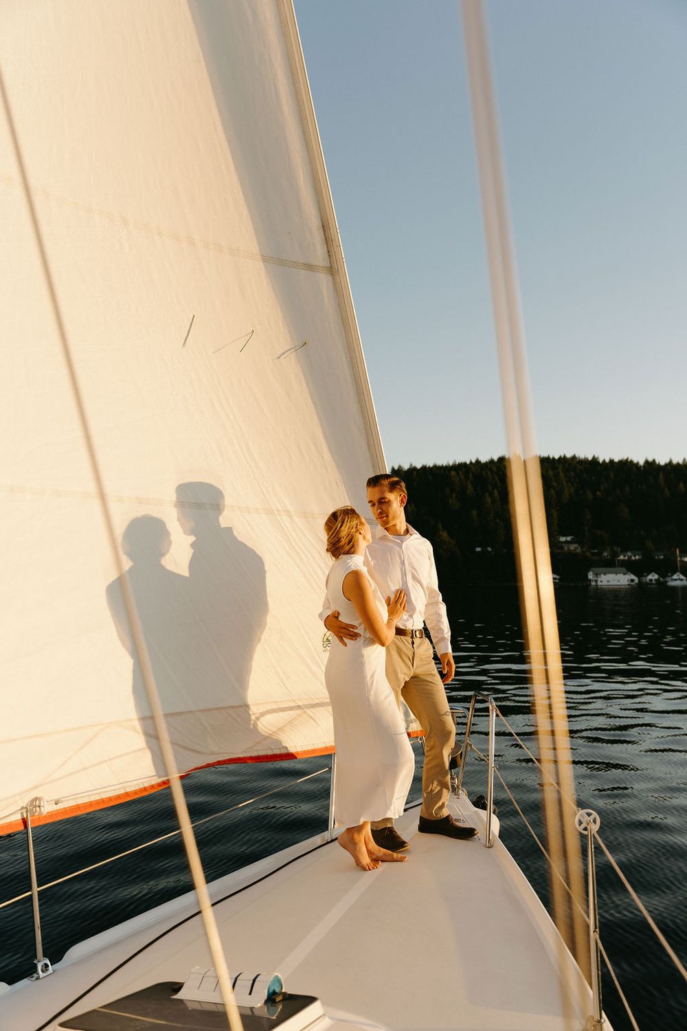 Couple standing on sailboat deck at sunset with their shadows cast against the white sail.