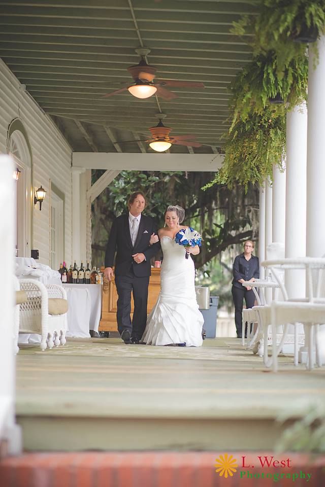 A wedding processional on an elegant white columned porch with hanging plants.